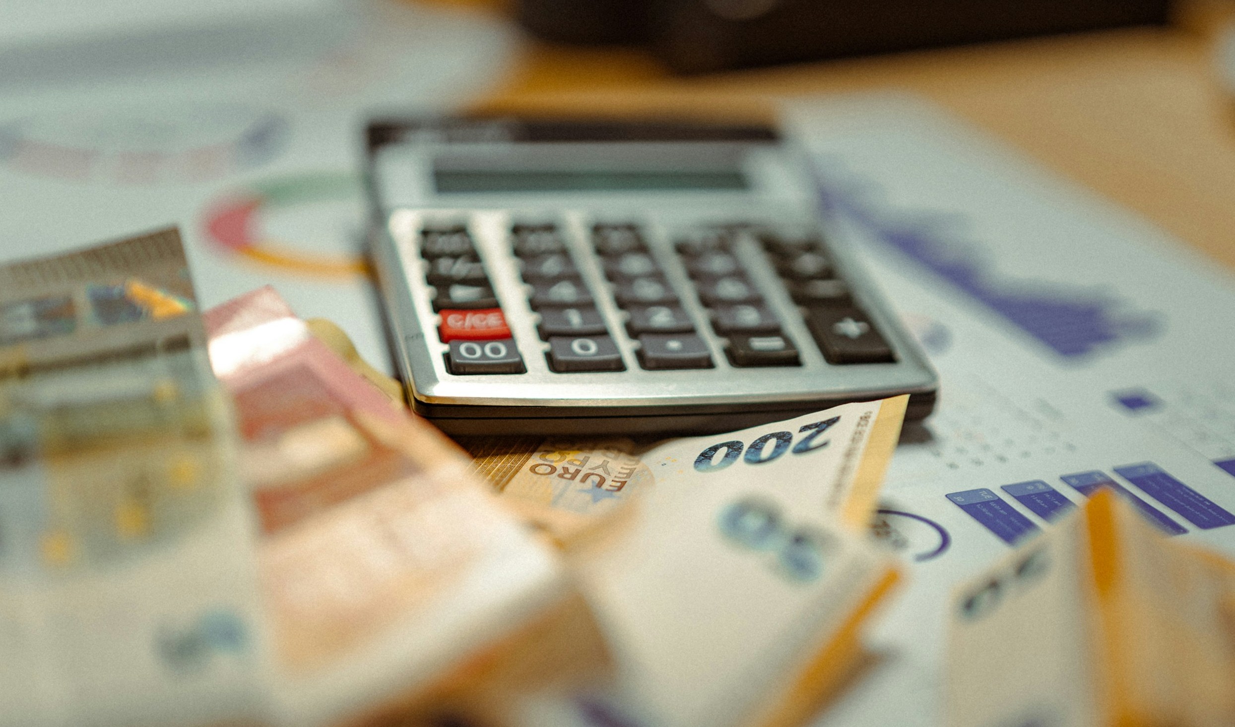 Calcolatrice e banconote in euro appoggiate su fogli con grafici e tabelle finanziarie