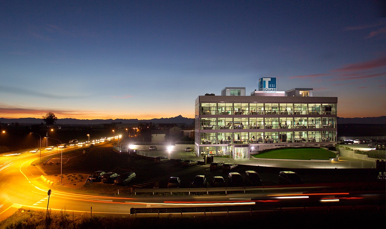 Edificio vetrato illuminato al tramonto con l’insegna Tesisquare sul tetto