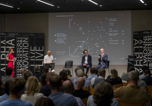 Relatori sul palco della quarta edizione di Alpha Innovation Live al NOI Techpark di Bolzano, con lo schermo che mostra i risultati della survey sui partecipanti