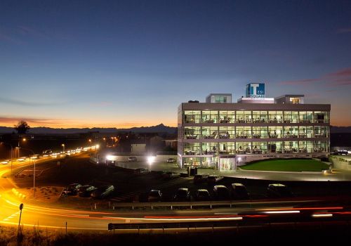Edificio vetrato illuminato al tramonto con l’insegna Tesisquare sul tetto